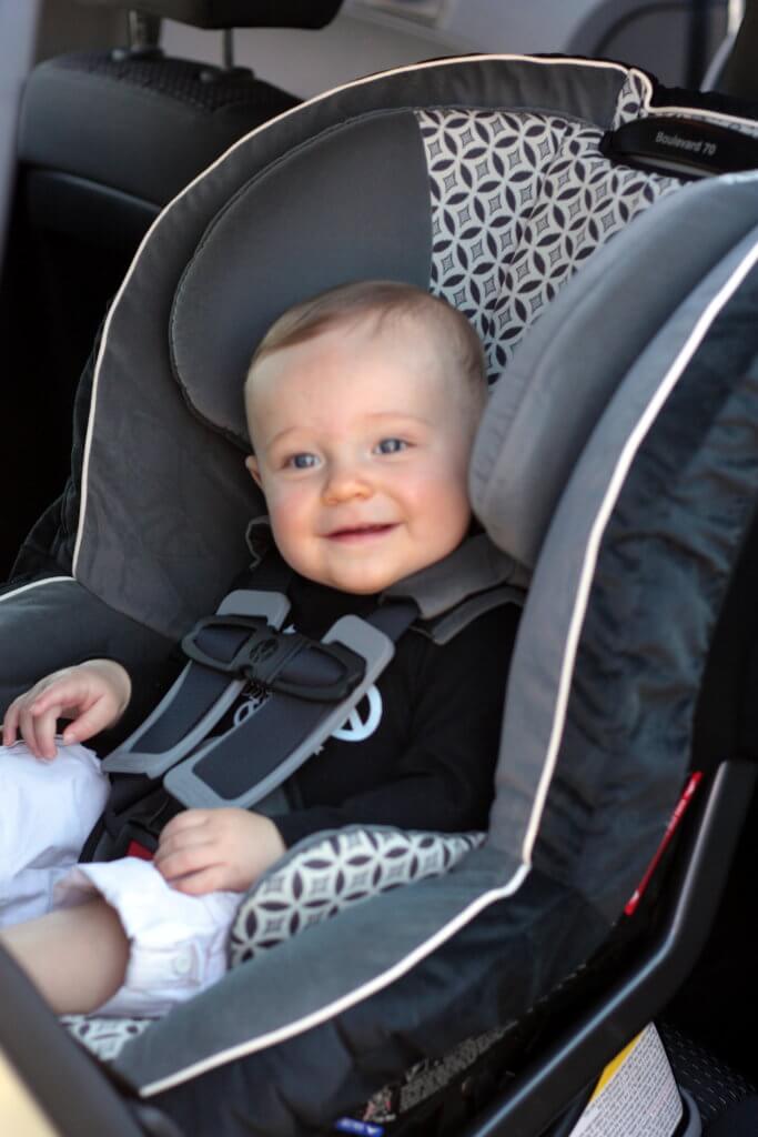 Six month old baby strapped into a car seat in the backseat of a car.