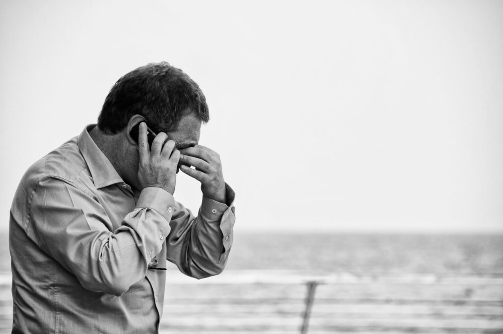 Worried man talking on the phone at the beach.