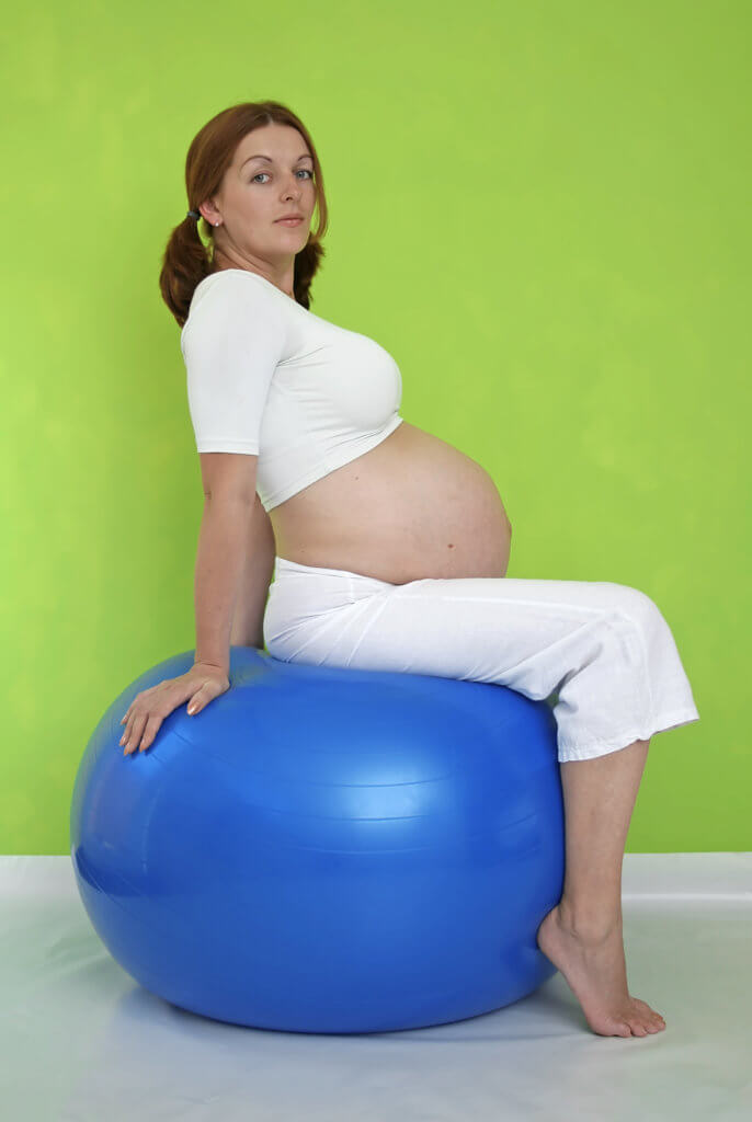 Pregnant woman sitting on a blue exercise ball.