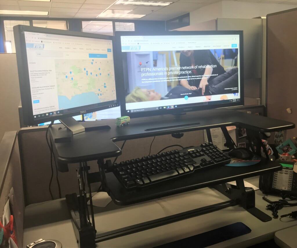 Photograph of a standing desk set up, where the computer, keyboard and mouse are on a platform that can be adjusted in height pending whether you are sitting or standing.