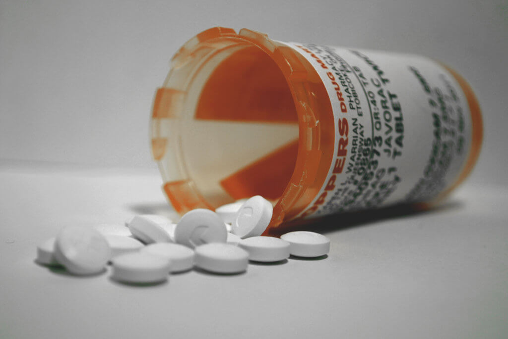 Photograph of a knocked-over prescription bottle with pills spilling out.