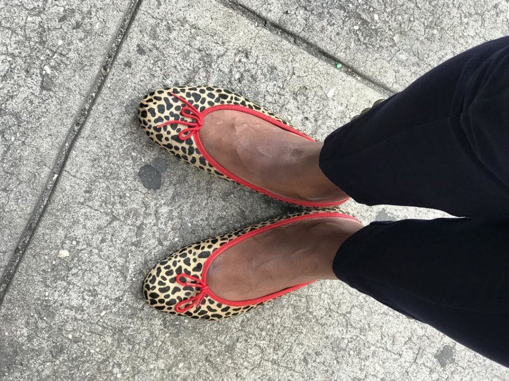 Legs and feet of woman wearing leopard print flats and black pants.