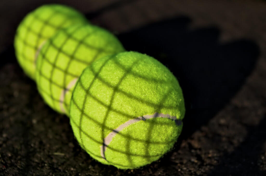 Three tennis balls that show the shadow of the net above them.