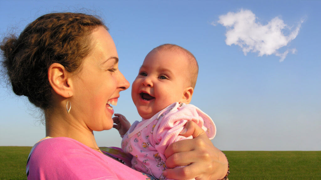Happy mother holding her smiling baby while outside.