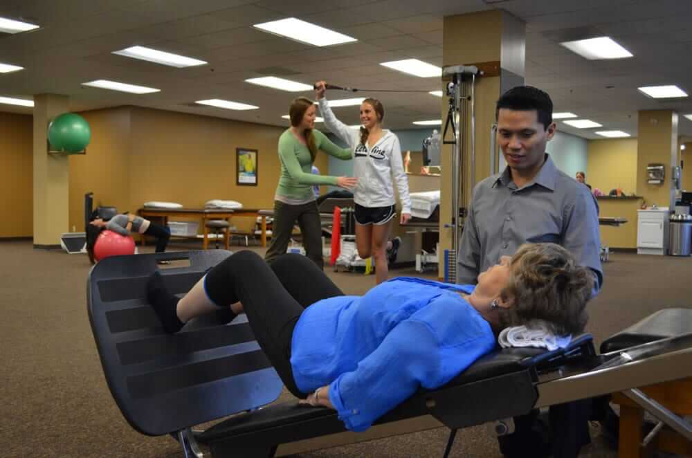 Male physical therapist working with older female patient to strengthen her legs.