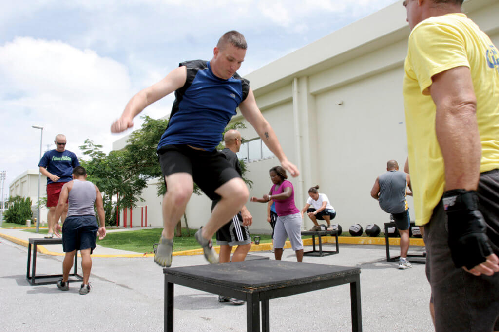 U.S. Marines doing plyometrics as part of their training outside. Photograph focuses on a man jumping from the street onto a box under the supervision of a trainer.