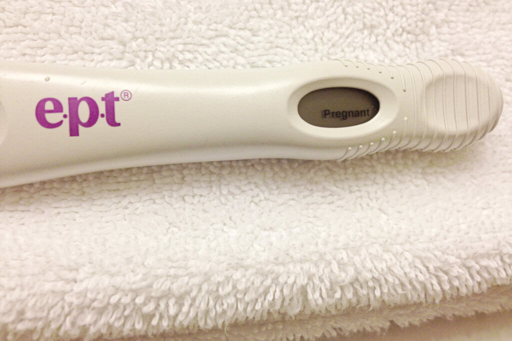 Positive EPT pregnancy test sitting on a white fluffy towel.