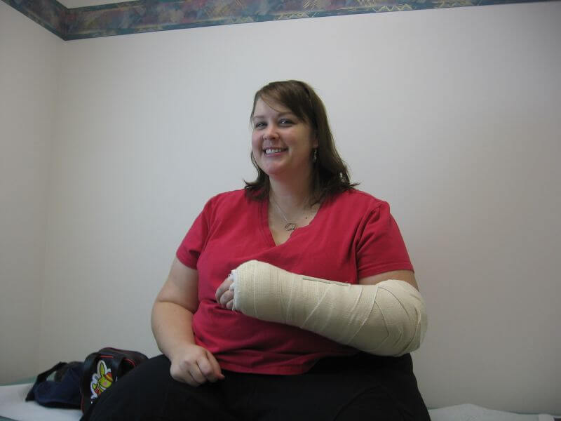 Overweight woman smiles and shows off her cast and bandages on her right wrist and forearm.