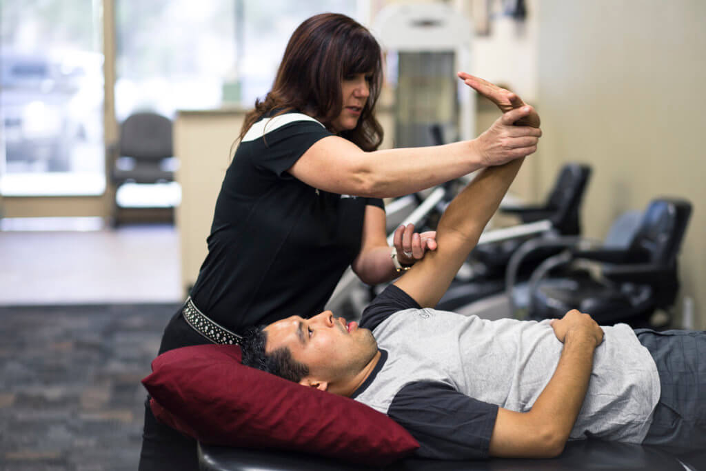 Female physical therapist helping male patient stretch his left forearm in order to strengthen in.