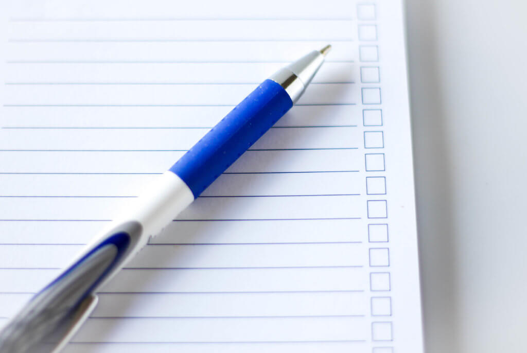 Notepad with blank lines for to do items and blank boxes to allow person to check off items. A blue mechanical pencil lies on top of the notepad.