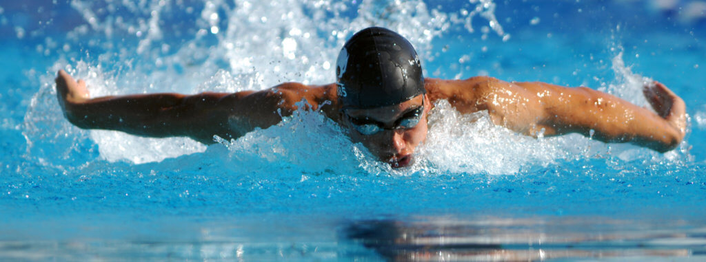 Man wearing a cap and goggles, swimming in a pool.