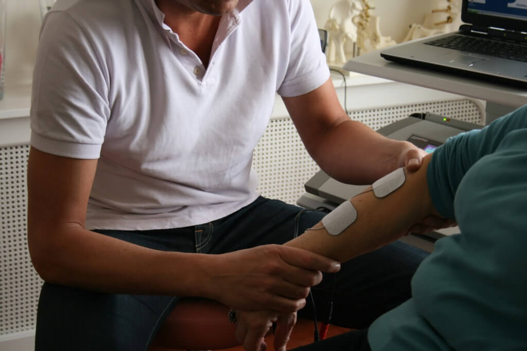 Male physical therapist using electrical stimulation to treat elbow pain of a patient.