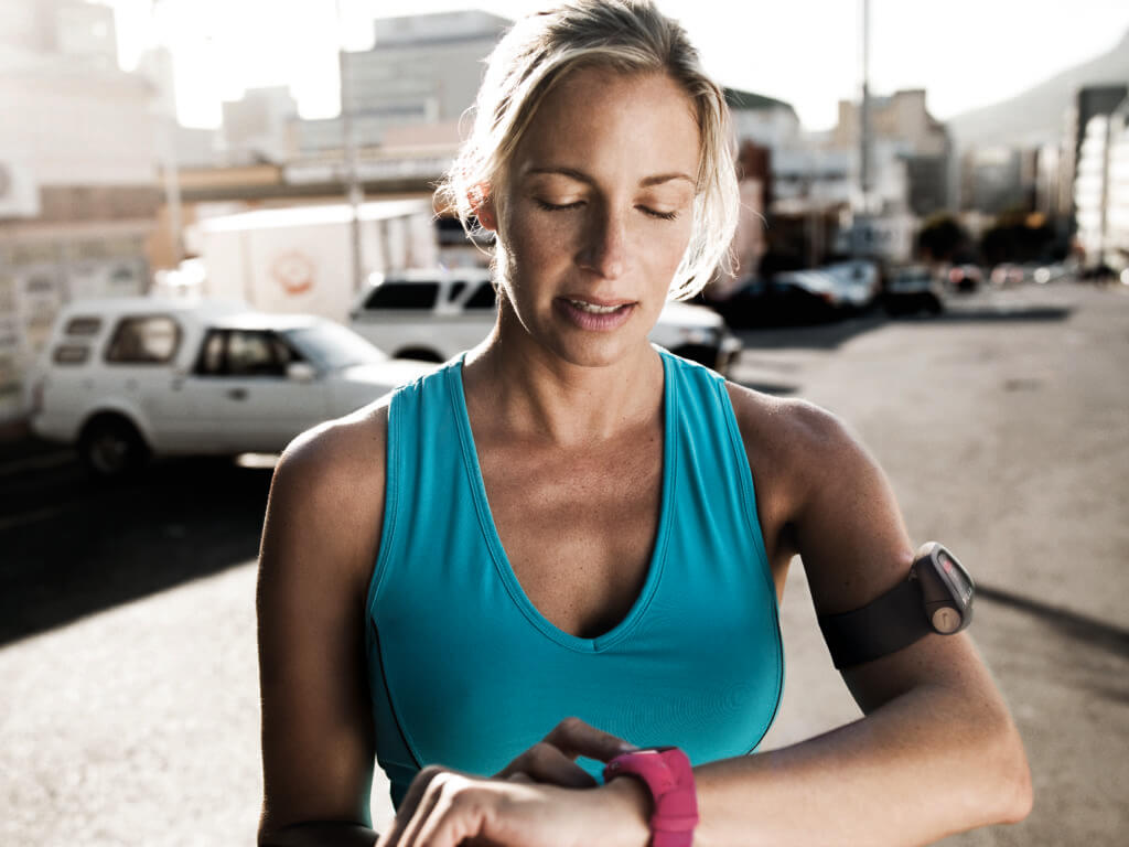 Blonde woman pausing during a run in the city to check her Polar watch for her heart rate.