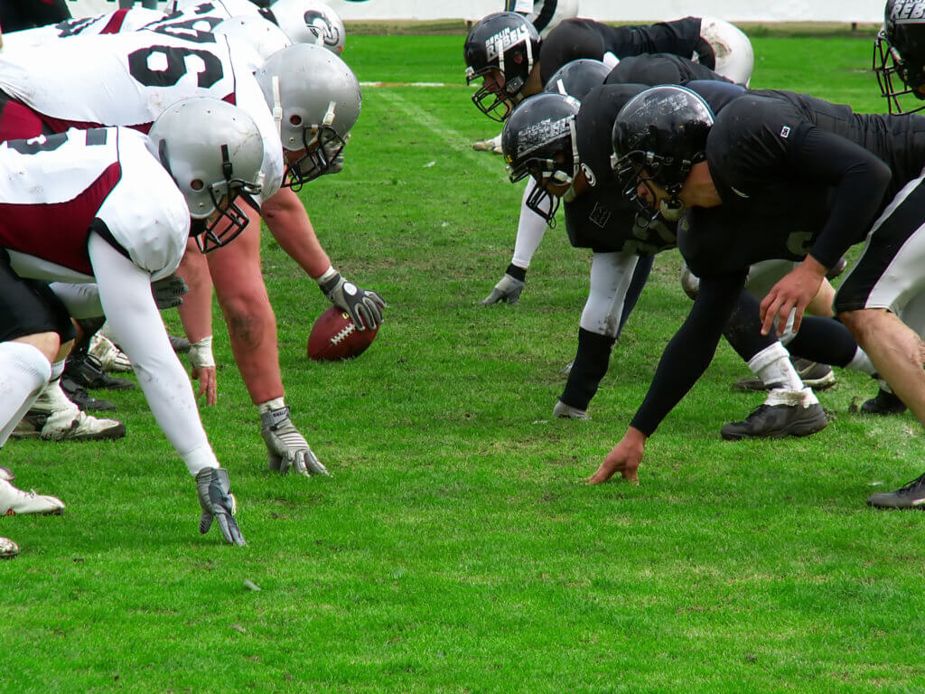 Photograph of two football teams lining up to face each other at the line of scrimmage on a football field.