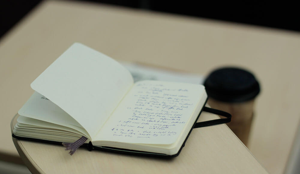 Photograph of a small notebook, opened on a table. Handwriting can be seen on the pages, but the writing is fuzzy and cannot be read.