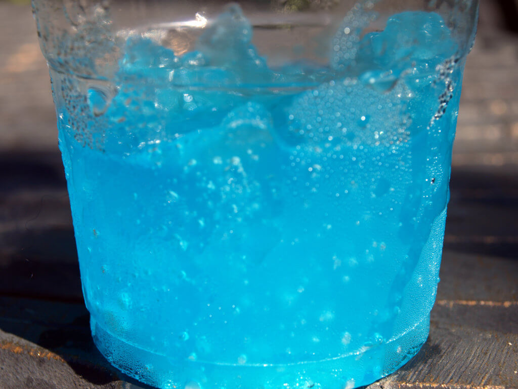 Photograph of a blue slushie in a clear plastic cup.