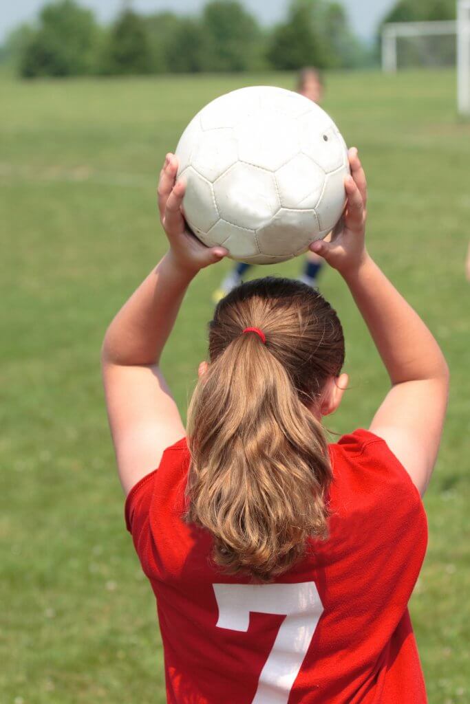 Back of teenage girl holding a white soccer ball over her head